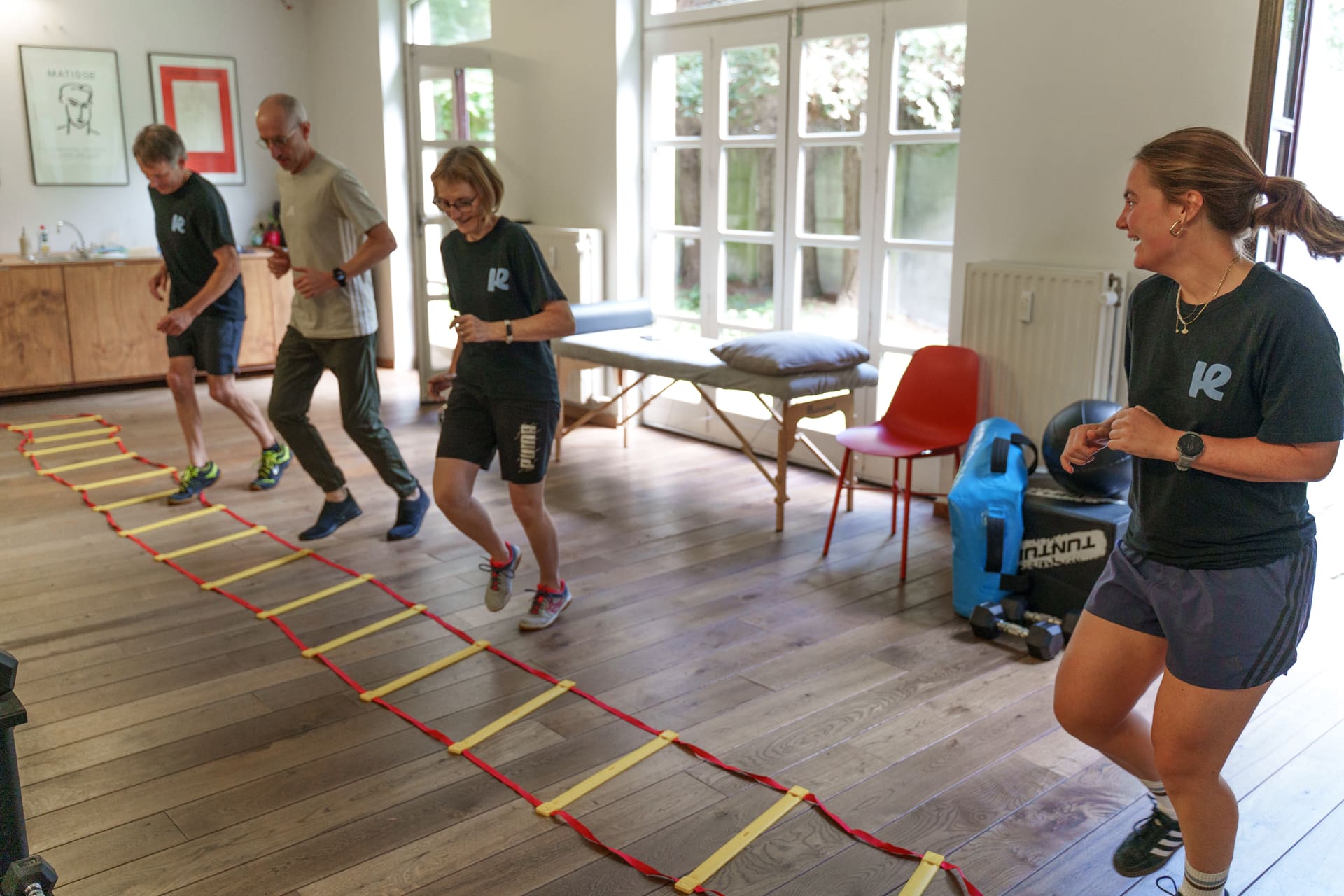 Vier deelnemers werken aan de speedladder tijdens een groepsles, de kinesitherapeute stuurt bij