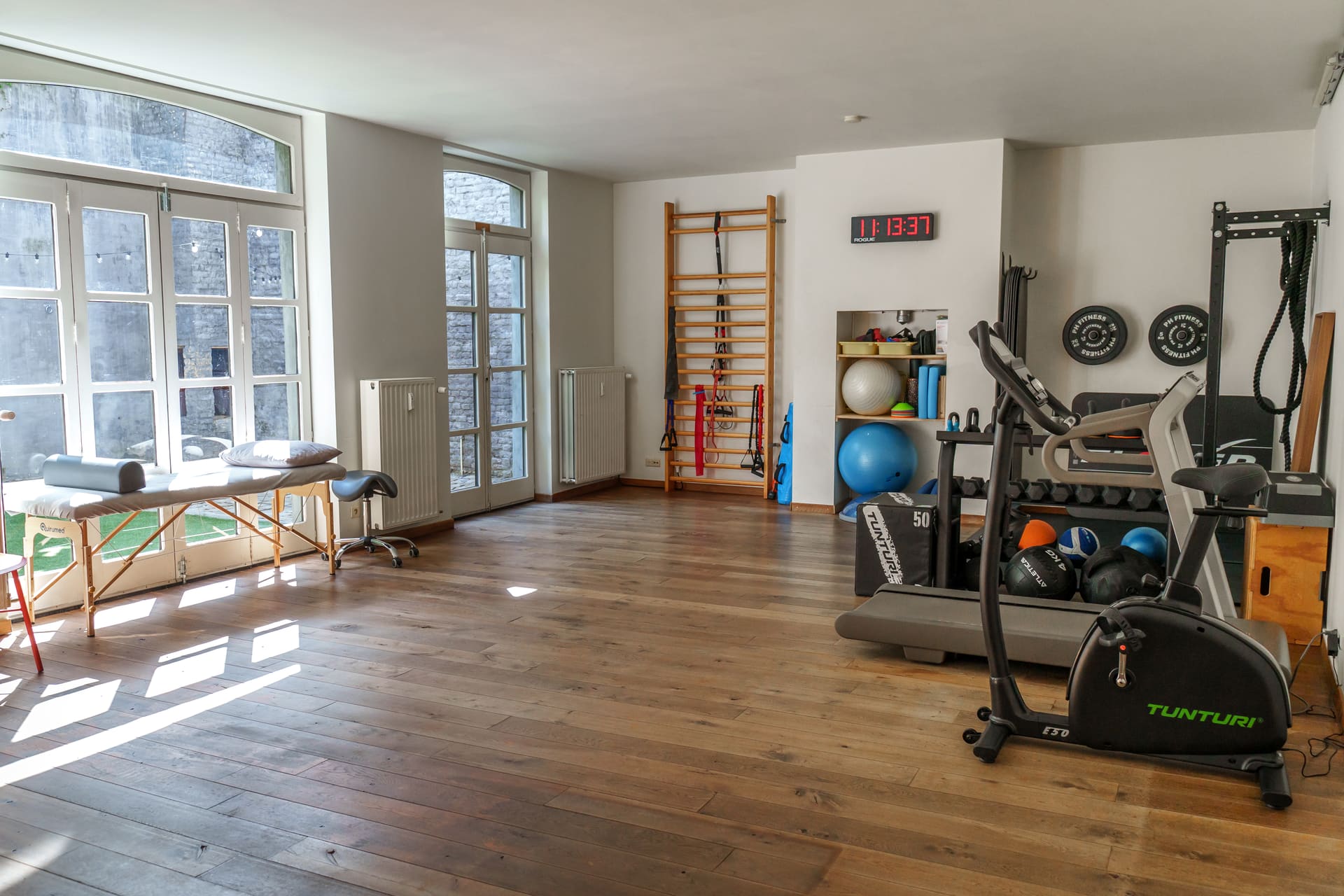 Oefenzaal met wandrek, crosstrainer en hometrainer bij daglicht